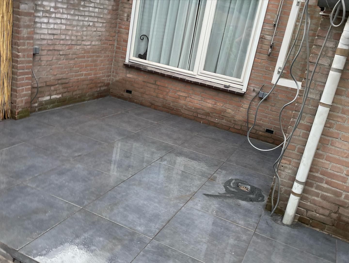 Terras met grote antraciet tegels tegen de gevel van de woning